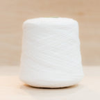 Cheekyarn Loop 8 yarn cone in Milk Tooth, a warm off-white, against a natural wood background
