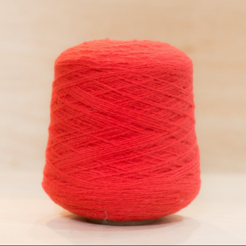 Cheekyarn Loop 8 yarn cone in Nosebleed, a vivid high-saturation red, against a natural wood background