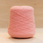 Cheekyarn Loop 8 yarn cone in Slap Cheek, a warm flushed medium pink, against a natural wood background