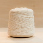 Cheekyarn Loop 8 yarn cone in Flour Face, a warm off-white, against a natural wood background