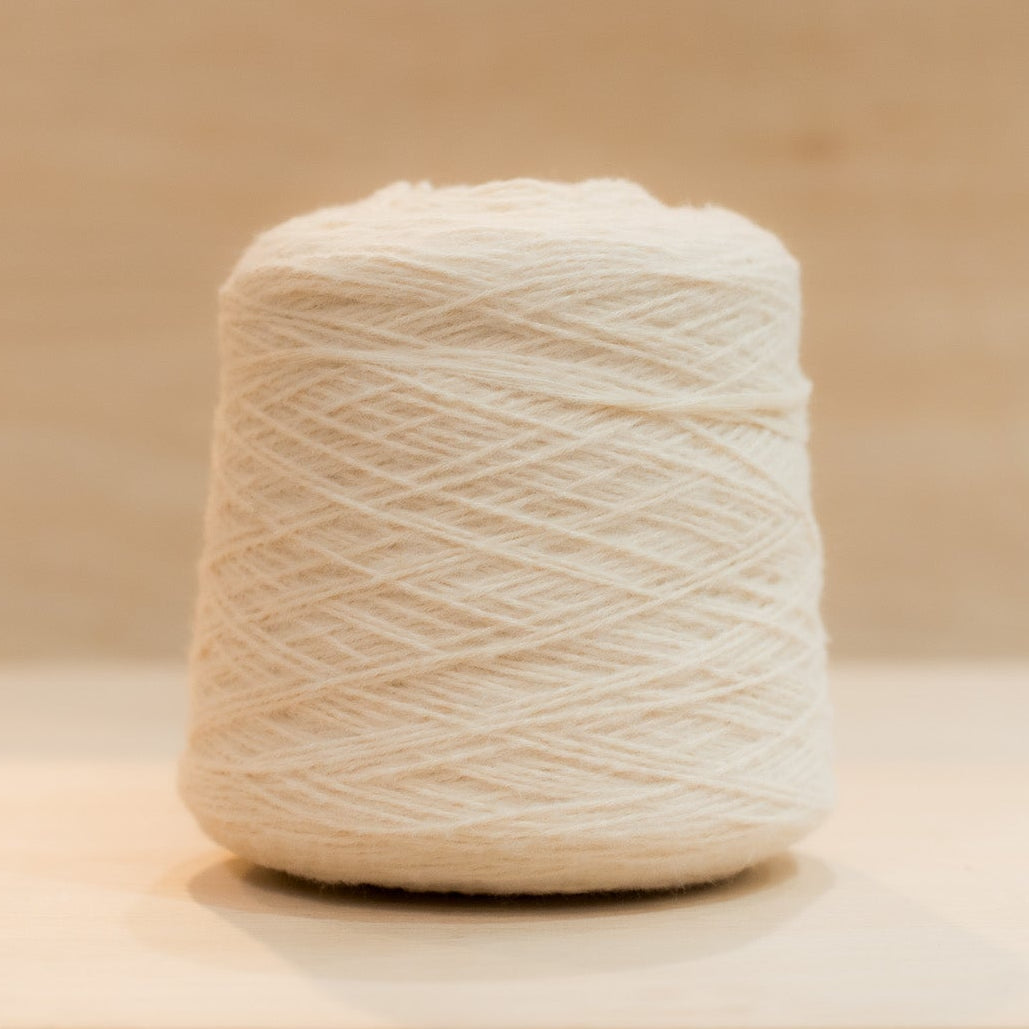 Cheekyarn Loop 8 yarn cone in Flour Face, a warm off-white, against a natural wood background