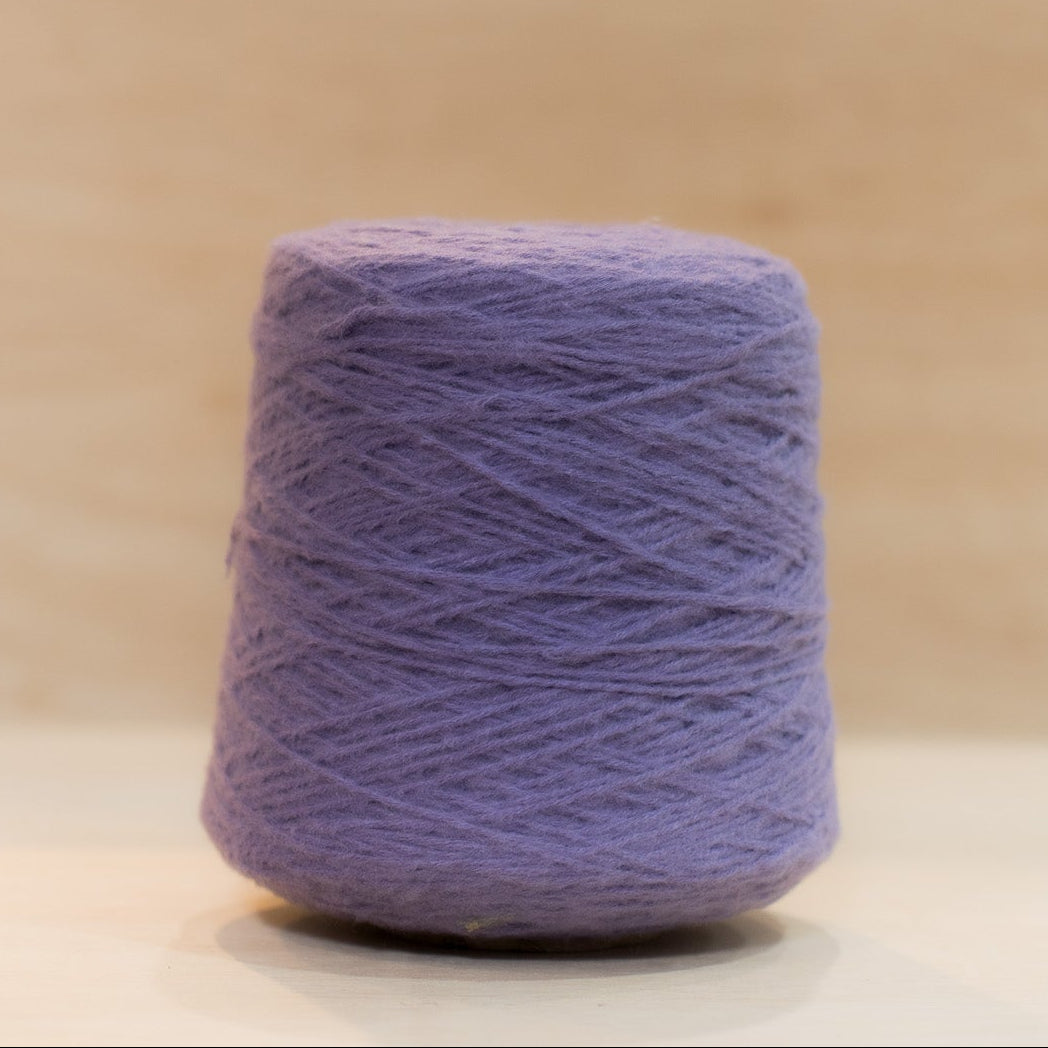 Cheekyarn Loop 8 yarn cone in Royal Bruise, a mid-toned blue-purple, against a natural wood background