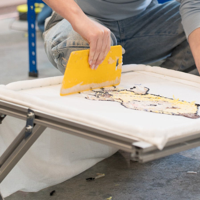 Woman working on a project in a workshop setting with shelves and tools in the background.